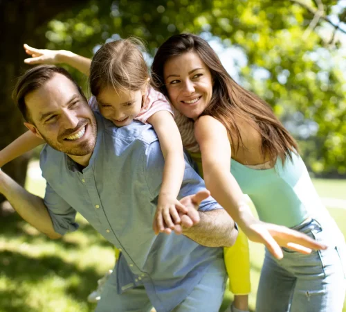 Happy young family with cute little daughter having fun in park on a sunny day